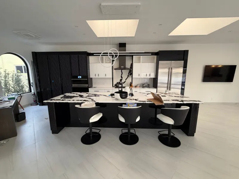 Black kitchen with island. Black tall cabinets across the back wall, white uppers and an island with a fluted base.